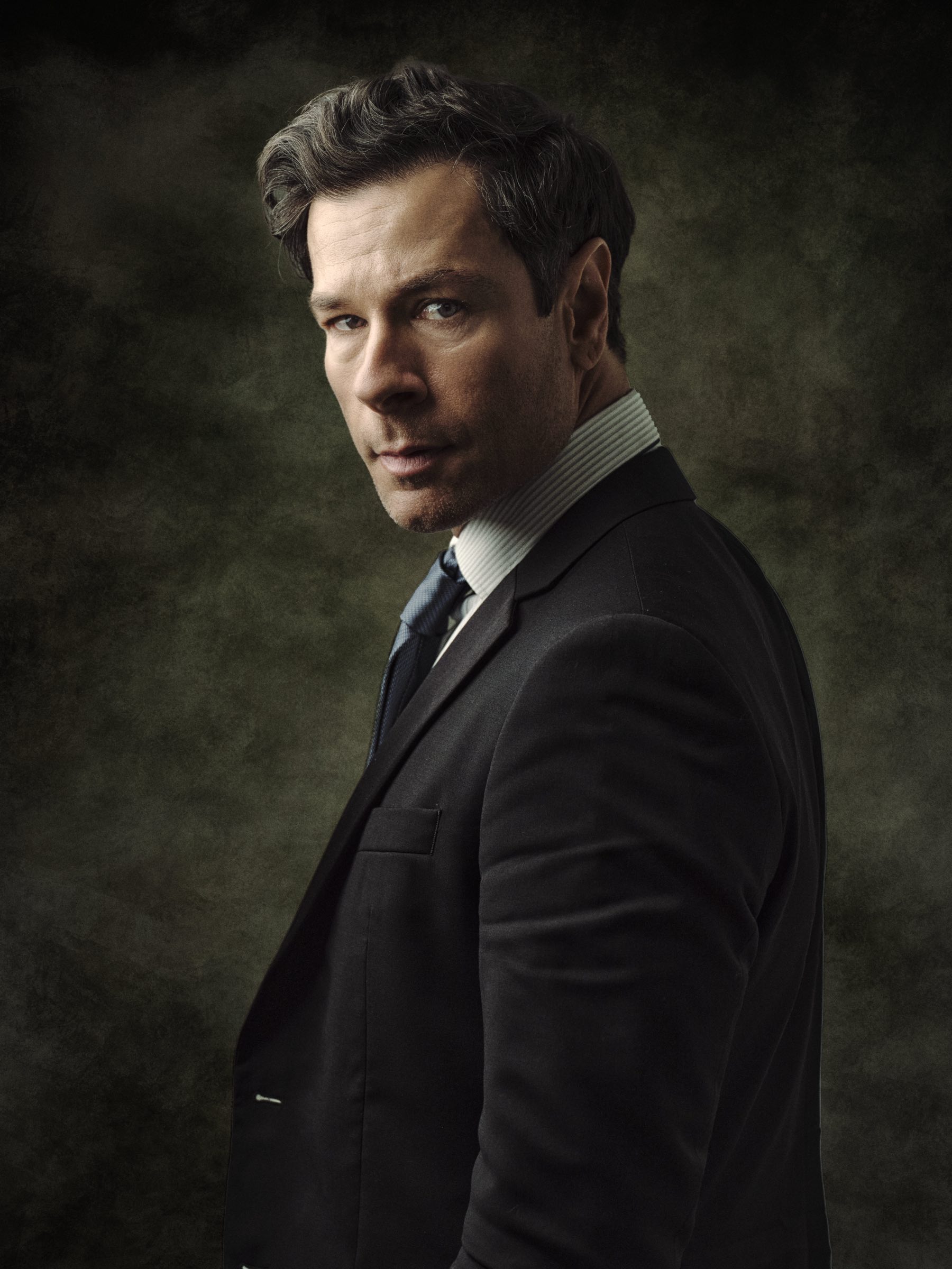 Moody editorial portrait of a man in a dark suit against a textured backdrop, photographed in Vancouver.